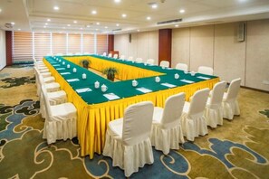 Un salón de conferencias con una larga mesa, sillas blancas y suelo alfombrado.