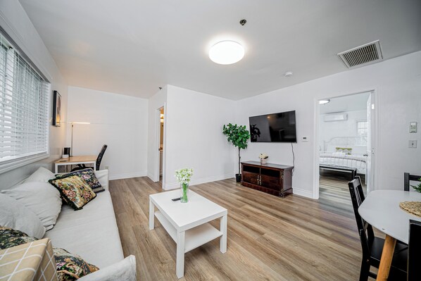 Een moderne woonkamer met een witte bank, een salontafel, een aan de muur bevestigde televisie en een houten vloer.