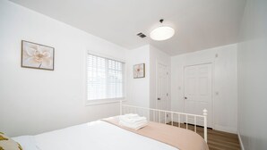 Un dormitorio con cama, ventana con persianas, puerta y lámpara de techo.