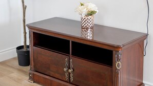 Un mueble de madera con centro de entretenimiento, un televisor montado en la pared, una planta en maceta y un florero con flores.