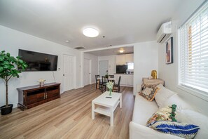 Een woonkamer met een witte bank, een salontafel, een televisie en een eethoek met stoelen en een tafel.