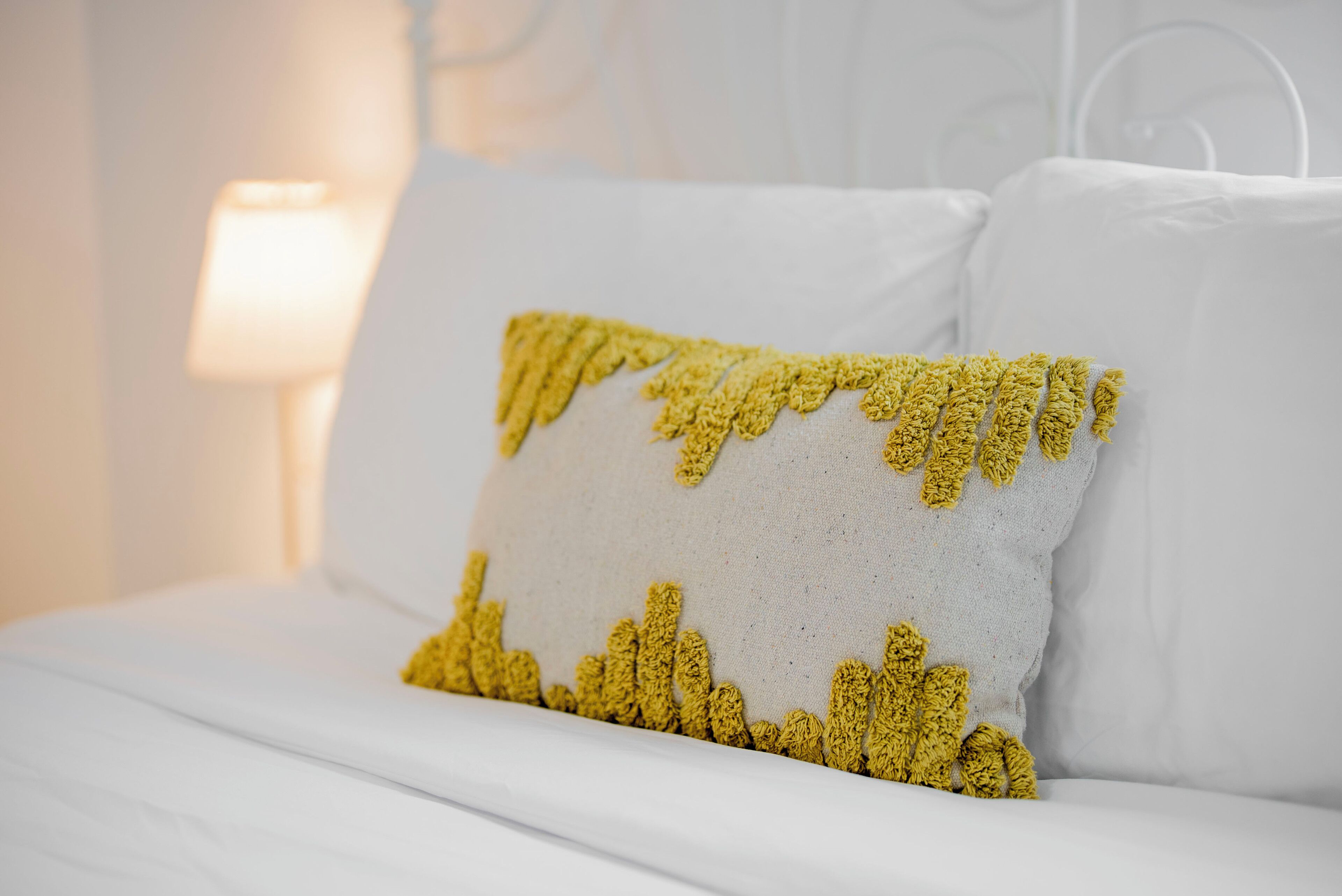 Un lit avec une literie blanche et un seul oreiller jaune à motifs texturés.