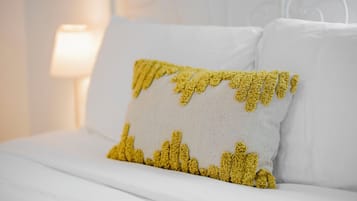 Una cama con ropa de cama blanca y una única almohada amarilla de diseño texturizado.
