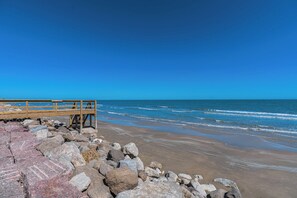 A beach with a wooden pier and rocky shoreline. - Charming updated Surfside home with firepit - only 2 min walk to the beach! (Surfside Beach)