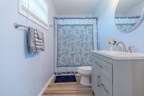 A bathroom with a toilet, sink, and a shower curtain with a blue and white pattern. - Charming updated Surfside home with firepit - only 2 min walk to the beach! (Surfside Beach)