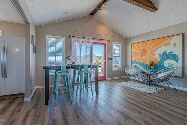 A kitchen with a bar area, wooden flooring, and a large window with blinds. - Charming updated Surfside home with firepit - only 2 min walk to the beach! (Surfside Beach)