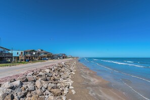 A beachside road with a rocky barrier, beachfront properties, and ocean views. - Charming updated Surfside home with firepit - only 2 min walk to the beach! (Surfside Beach)