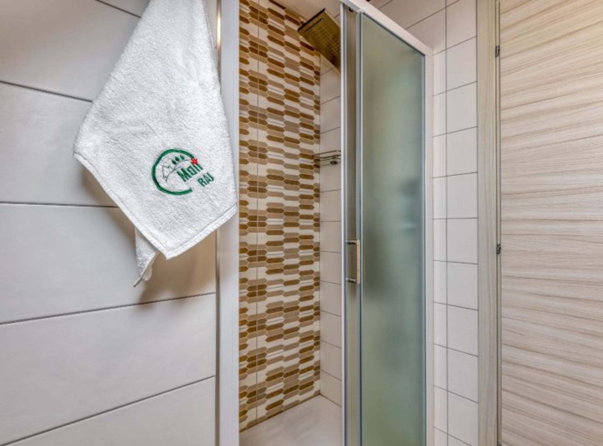 A bathroom with a white towel hanging on the wall, a patterned shower curtain, and a glass shower door.
