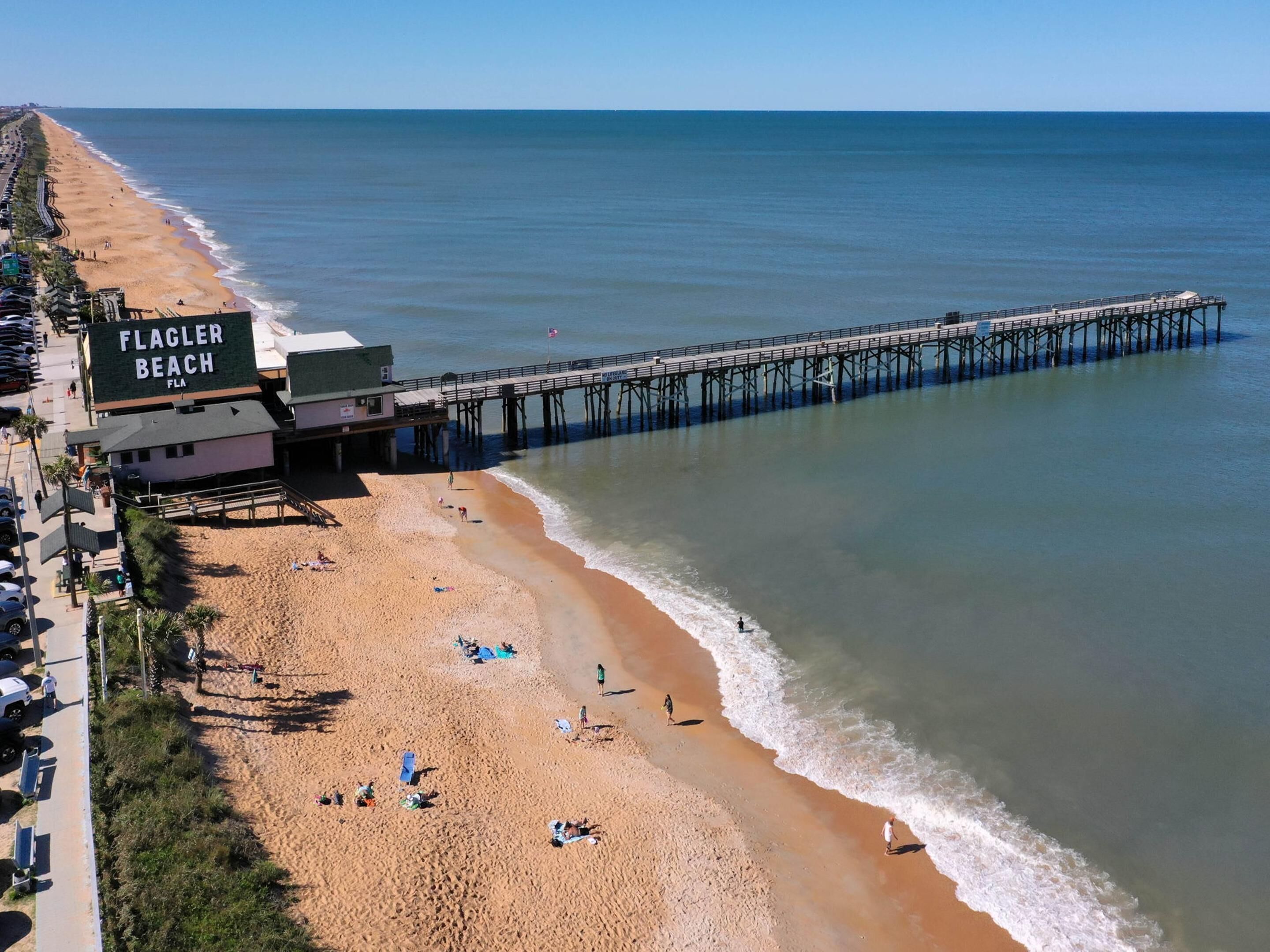 Une plage avec une jetée qui s’avance dans l’eau, portant l’inscription « FLAGLER BEACH ».