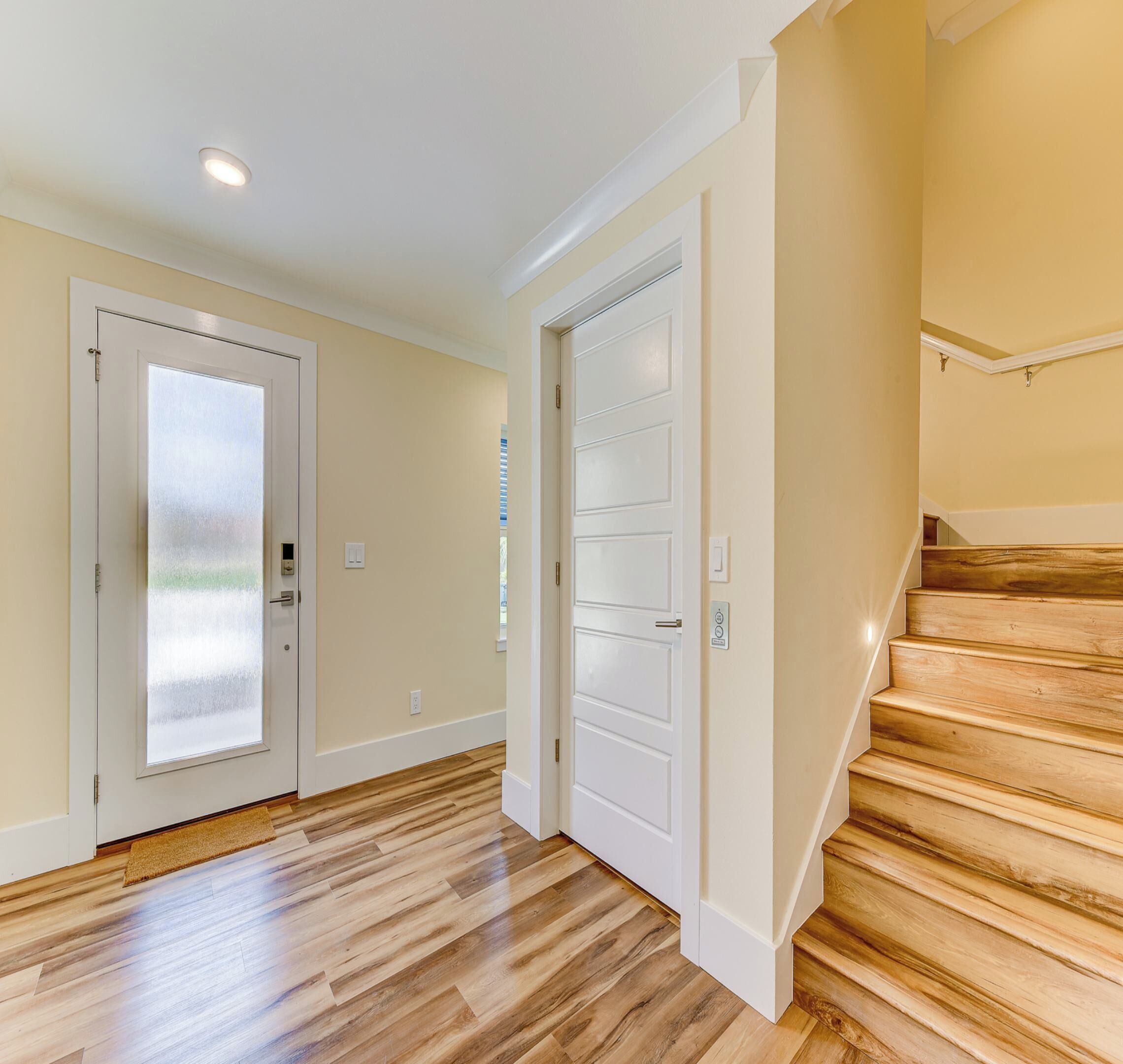Un couloir doté d’un plancher en bois, de deux portes blanches et d’un escalier en bois.