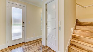 A hallway with wooden flooring, two white doors, and a wooden staircase. - Atlantic Beach House by Distinctive Beach Rentals (Flagler Beach)