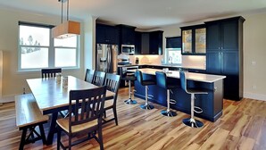 A modern kitchen with dark cabinets, a wooden dining table, and bar stools. - Atlantic Beach House by Distinctive Beach Rentals (Flagler Beach)