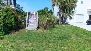 A private pathway marked by a wooden sign, surrounded by well-maintained grass and palm trees, leading to a building with a modern design. - Atlantic Beach House by Distinctive Beach Rentals (Flagler Beach)