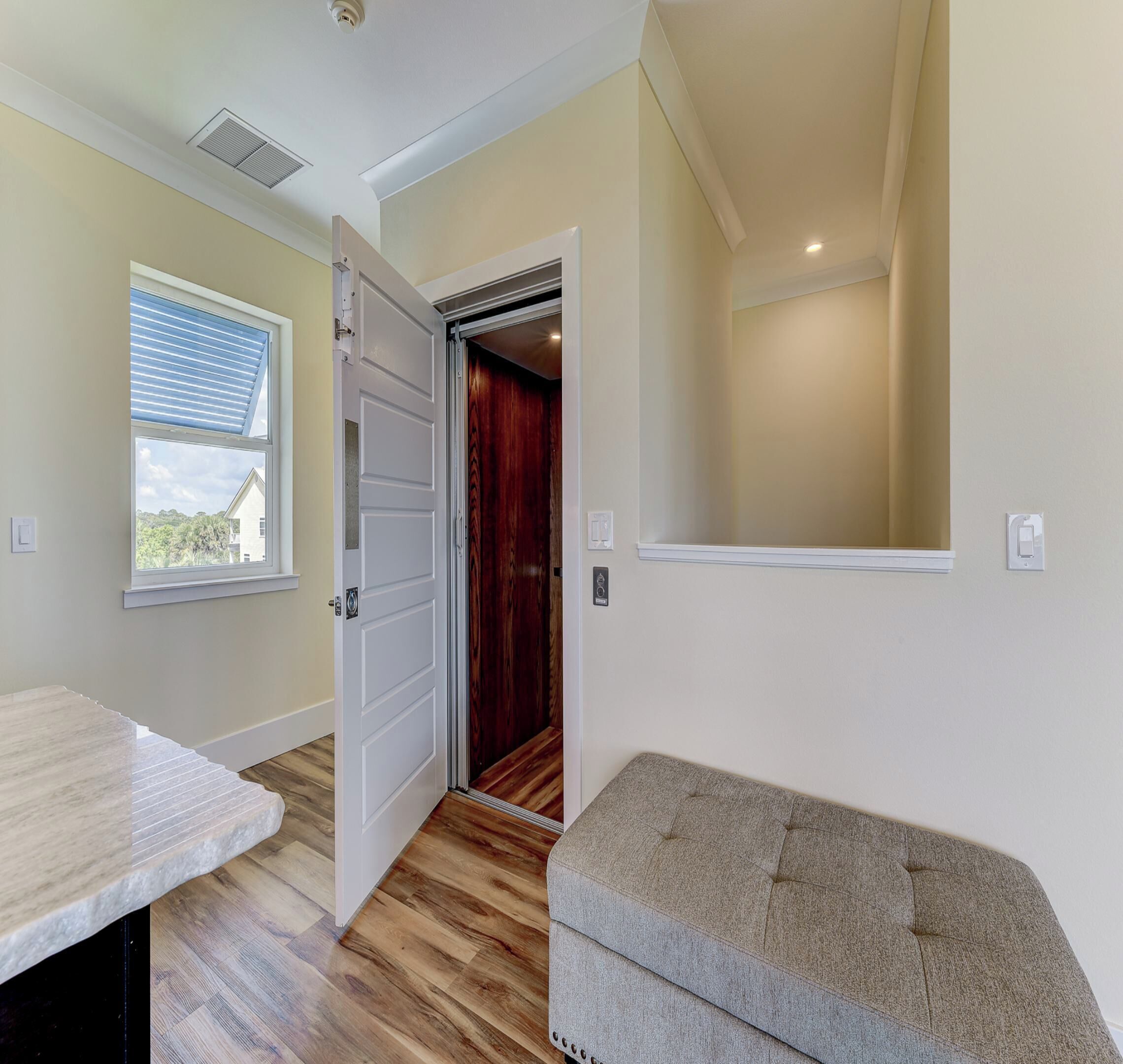 A room with a wooden floor, a bench, a door leading to a closet, and a window with blinds.