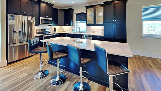 Una cocina moderna con armarios oscuros, electrodomésticos de acero inoxidable, una isla central con taburetes y suelo de madera.