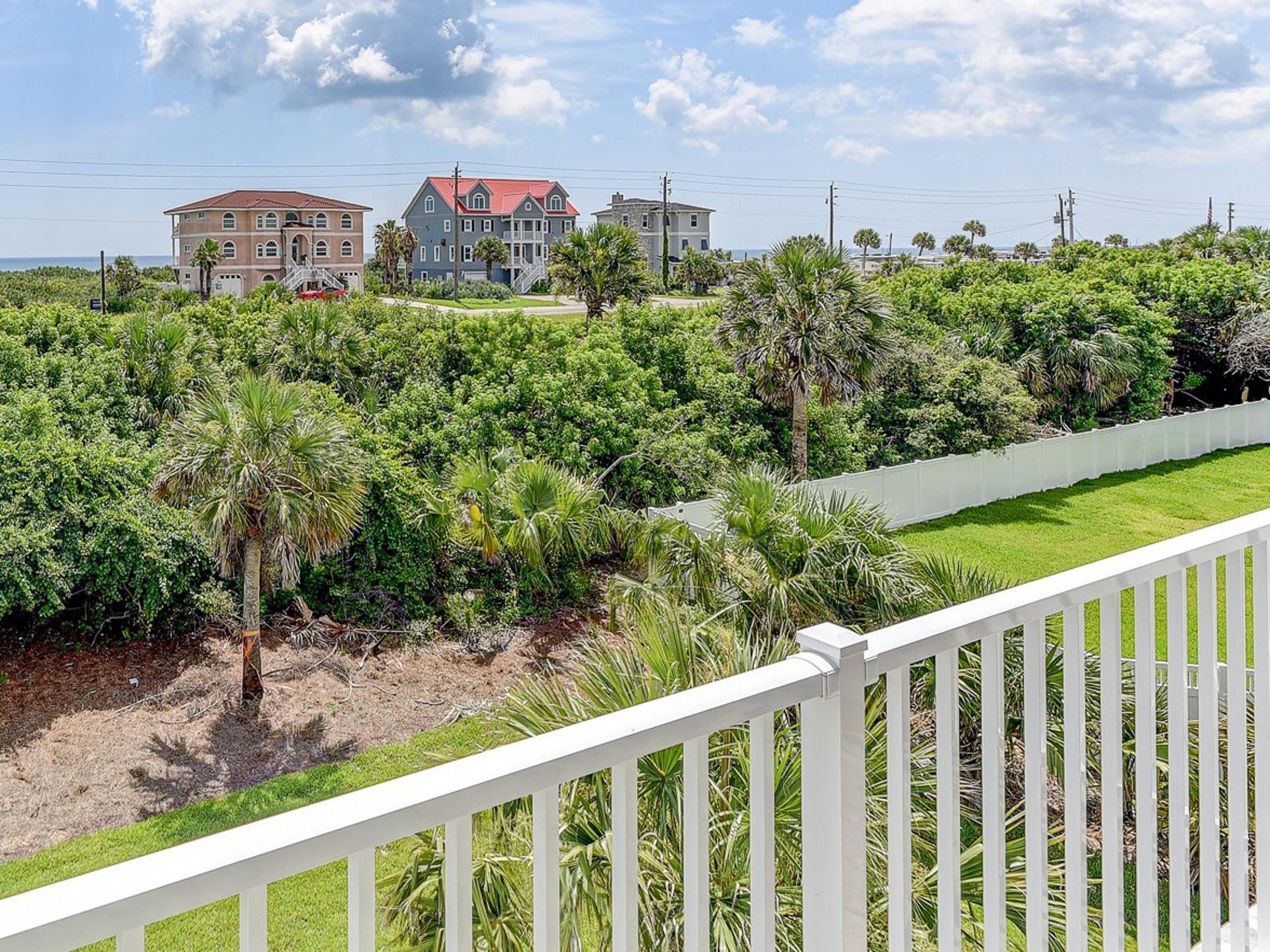 A coastal property with a large house, lush greenery, and a white fence.