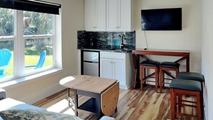 A compact kitchen with white cabinets, a black countertop, and a built-in refrigerator. There is a wooden dining table with two chairs and a TV mounted on the wall. - Atlantic Beach House by Distinctive Beach Rentals (Flagler Beach)