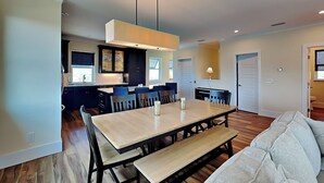 Una cocina moderna con armarios oscuros, una isla central y un comedor con mesa y bancos de madera.