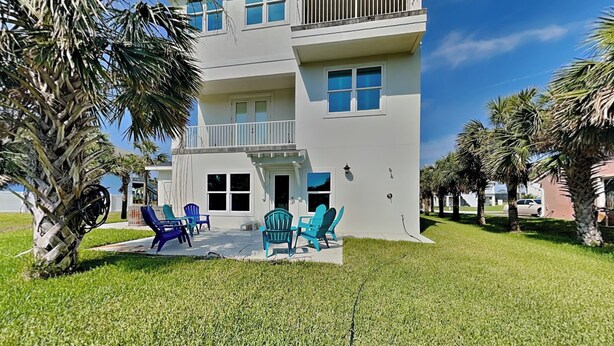 A two-story building with a balcony, a covered patio with chairs, and palm trees. - Atlantic Beach House by Distinctive Beach Rentals (Flagler Beach)
