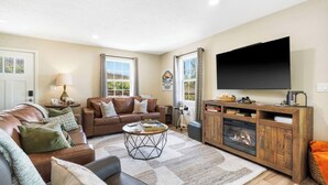 A living room with a brown leather sofa, a coffee table, a fireplace, and a television. - The Breakaway at Table Rock- Sauna, Hot Tub, Kayak, Full Upper and Lower Porches (Omaha)