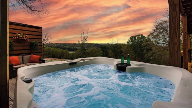 A hot tub with a view of a sunset and a wooden deck with outdoor seating. - The Breakaway at Table Rock- Sauna, Hot Tub, Kayak, Full Upper and Lower Porches (Omaha)