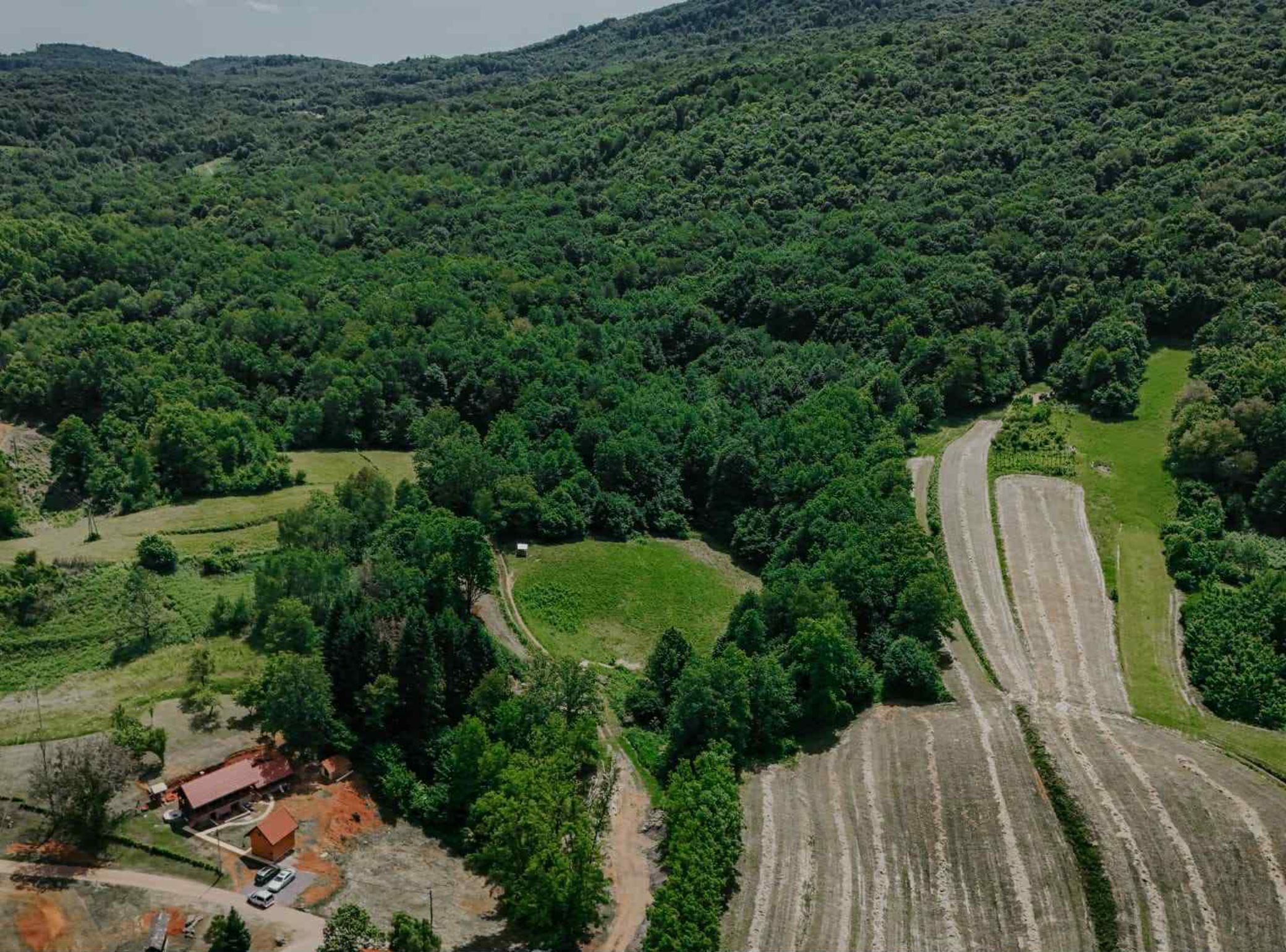 An aerial view of a rural area with a winding road, green fields, and scattered buildings.