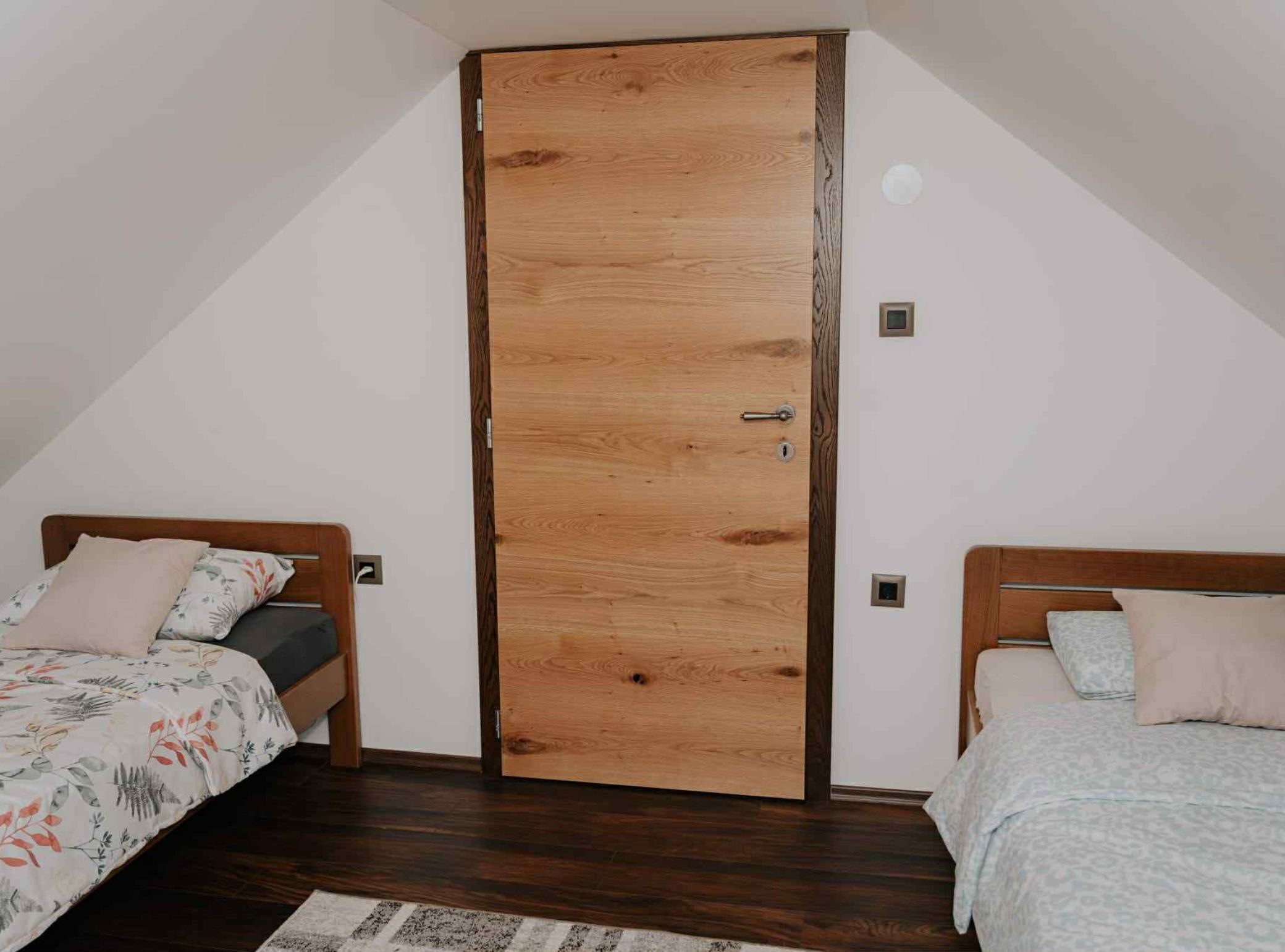 A bedroom with two beds, wooden flooring, and a wooden door.