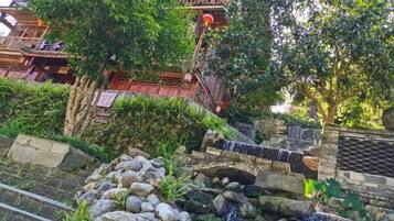 A traditional building with a stone bridge, lush greenery, and a waterfall.