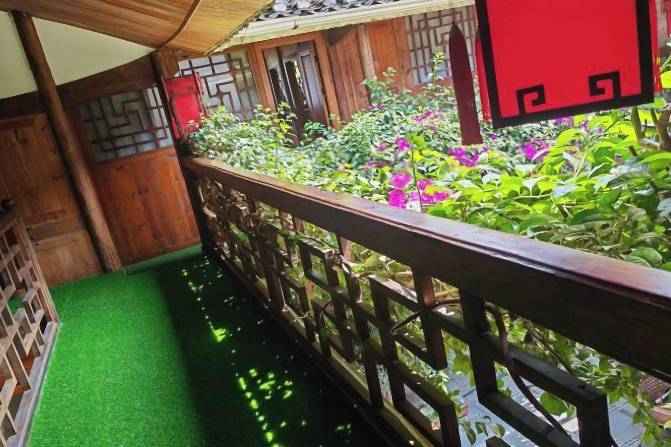 A wooden balcony with a green artificial turf floor, surrounded by lush plants and flowers.