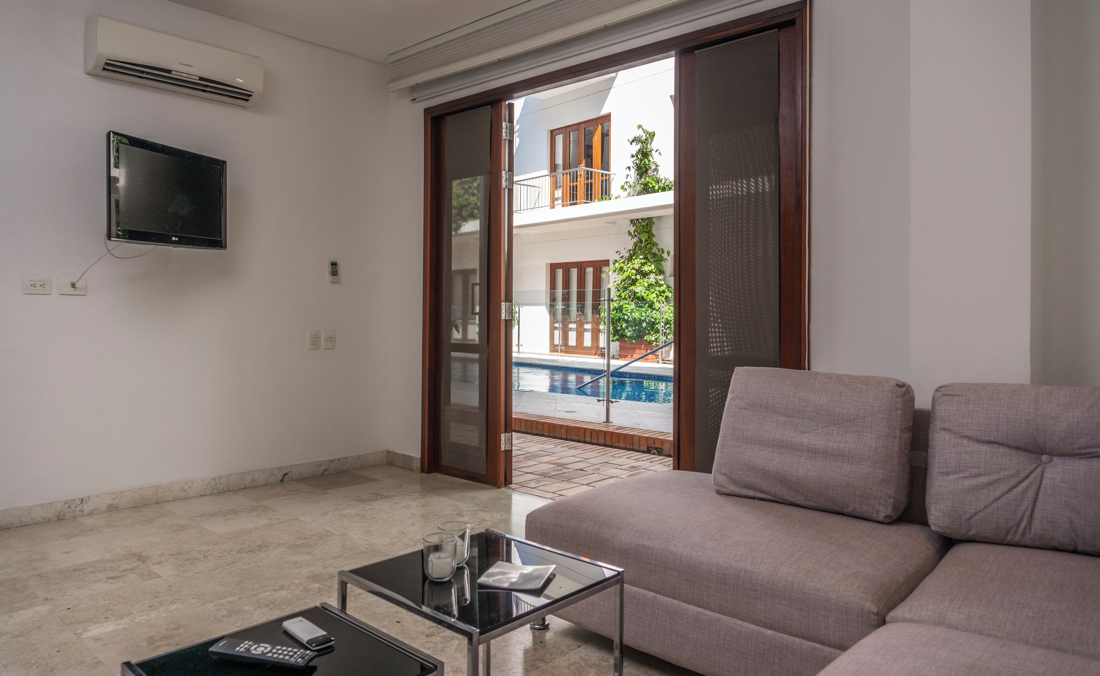 A living room with a sofa, a glass coffee table, and a flat-screen TV mounted on the wall.