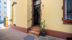 A yellow building with a black door, a small potted plant, and a metal handrail on the steps. - Apartment in Koblenz Near Deutsches Eck (Koblenz)