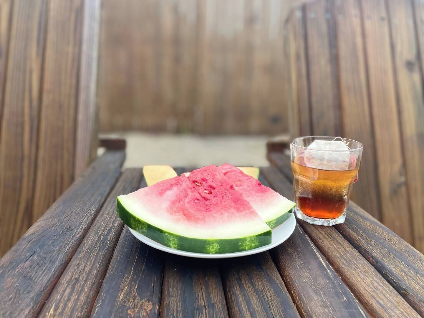 Ein Holztisch mit einer Schüssel Wassermelone und einem Glas Eistee.