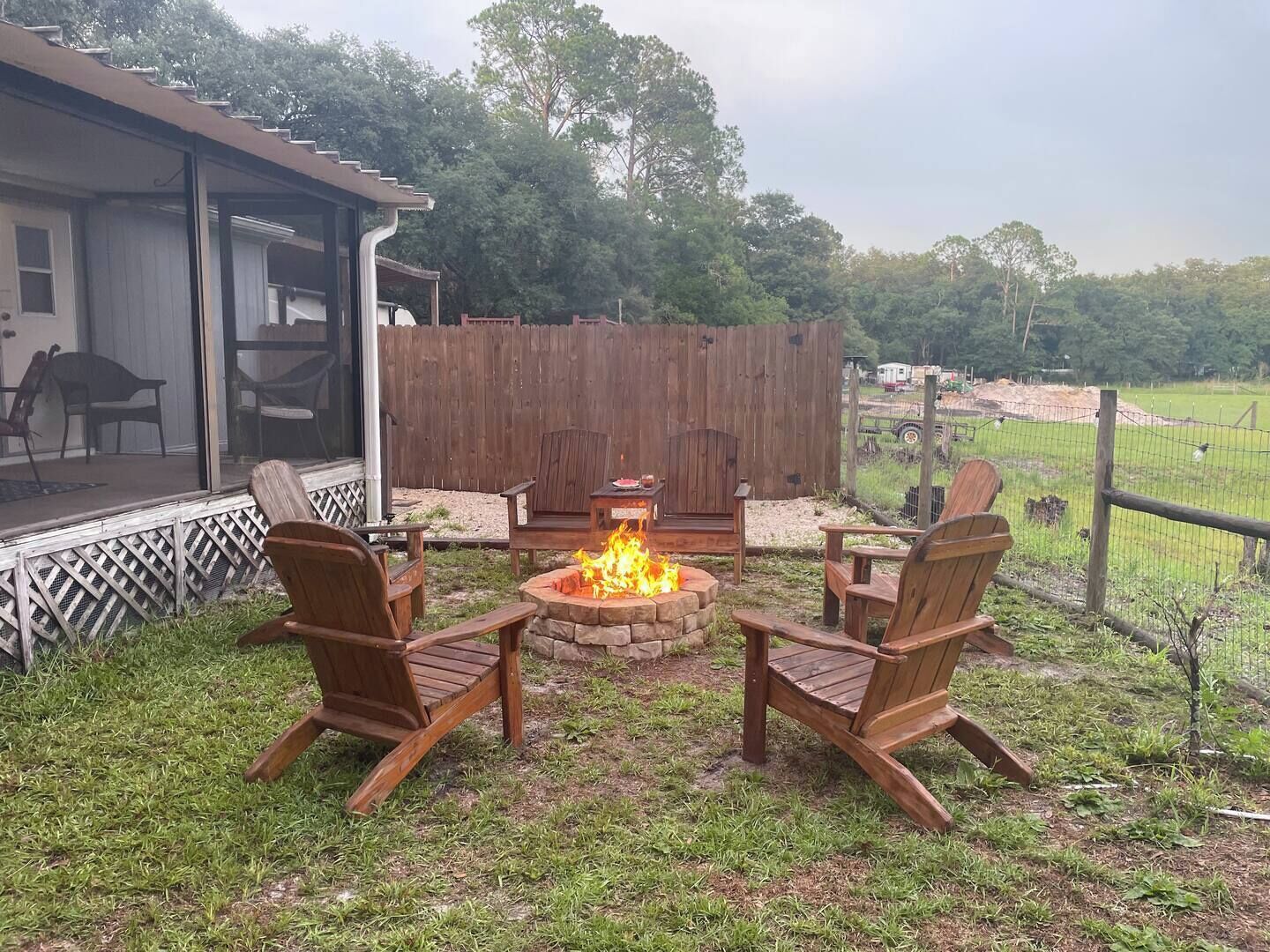 An outdoor patio with a fire pit, wooden chairs, and a covered seating area.