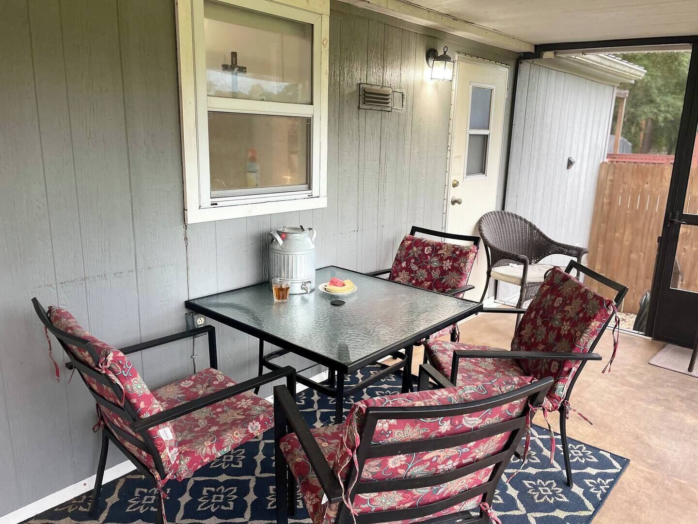 Un patio techado con una mesa y sillas, un farol de metal y una puerta que da a un espacio al aire libre.