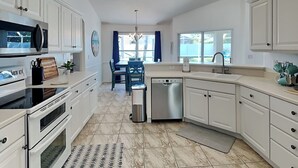 Een moderne keuken met witte kastjes, een roestvrijstalen vaatwasser en een eethoek met blauwe stoelen.