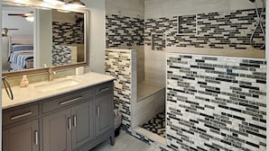 Une salle de bain moderne dotée d’un grand miroir, de deux vasques et d’un espace douche dont les murs sont recouverts de mosaïques.