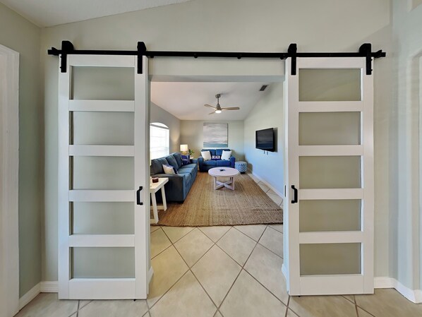 A spacious living area with a large sliding door, a sofa set, a coffee table, and a television. - Endless Summer by Distinctive Beach Rentals (Palm Coast)