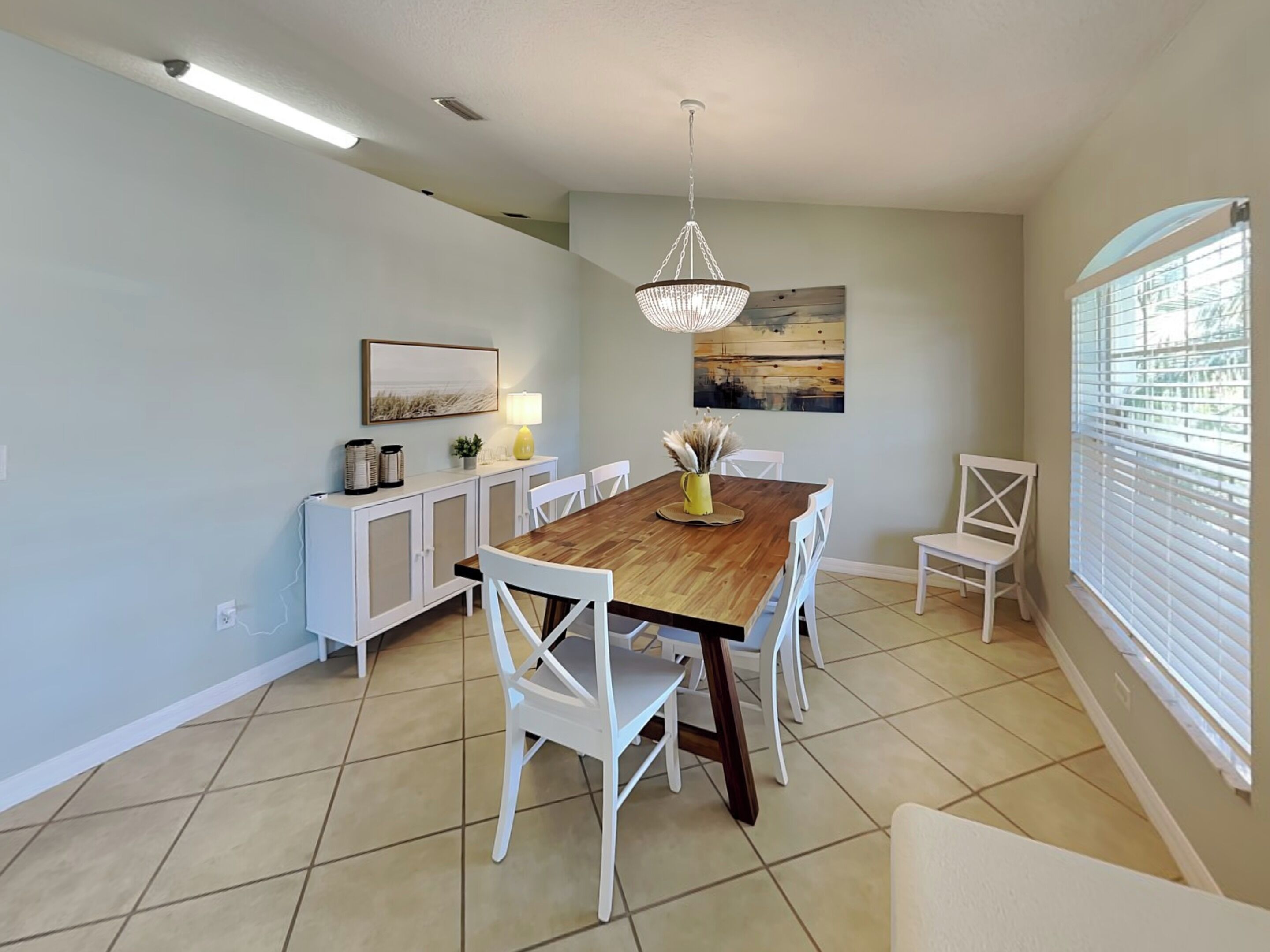 A dining area with a wooden table, white chairs, a chandelier, and artwork on the walls.