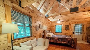 Ein gemütliches Schlafzimmer in einer Holzhütte mit Bett, Sofa und einem Fenster mit Jalousien.