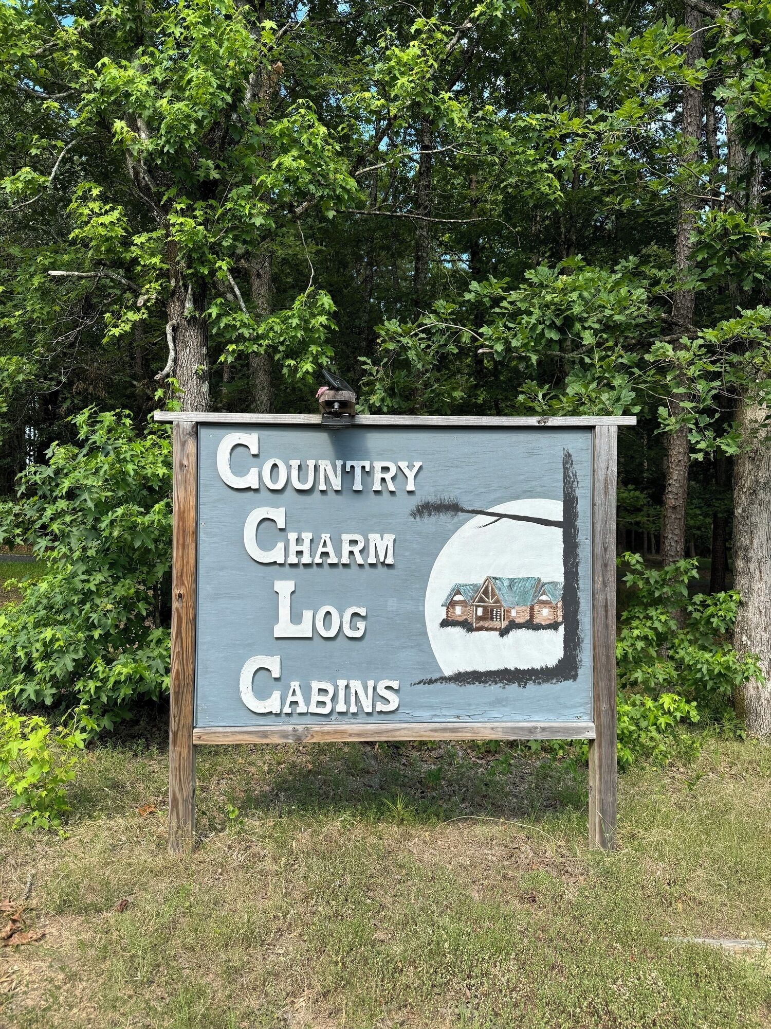 A sign for Country Charm Log Cabins with a cabin illustration.