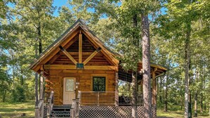 Eine Holzhütte mit Veranda und einem umzäunten Deck, umgeben von Bäumen.