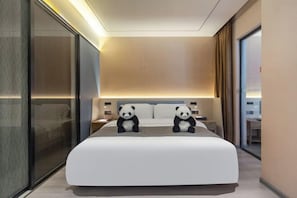 A modern hotel room with a large bed, two panda plush toys, a glass partition, and a nightstand with a lamp. - YinShu Hotel(Chengdu Panda BaseStore) (Chengdu)