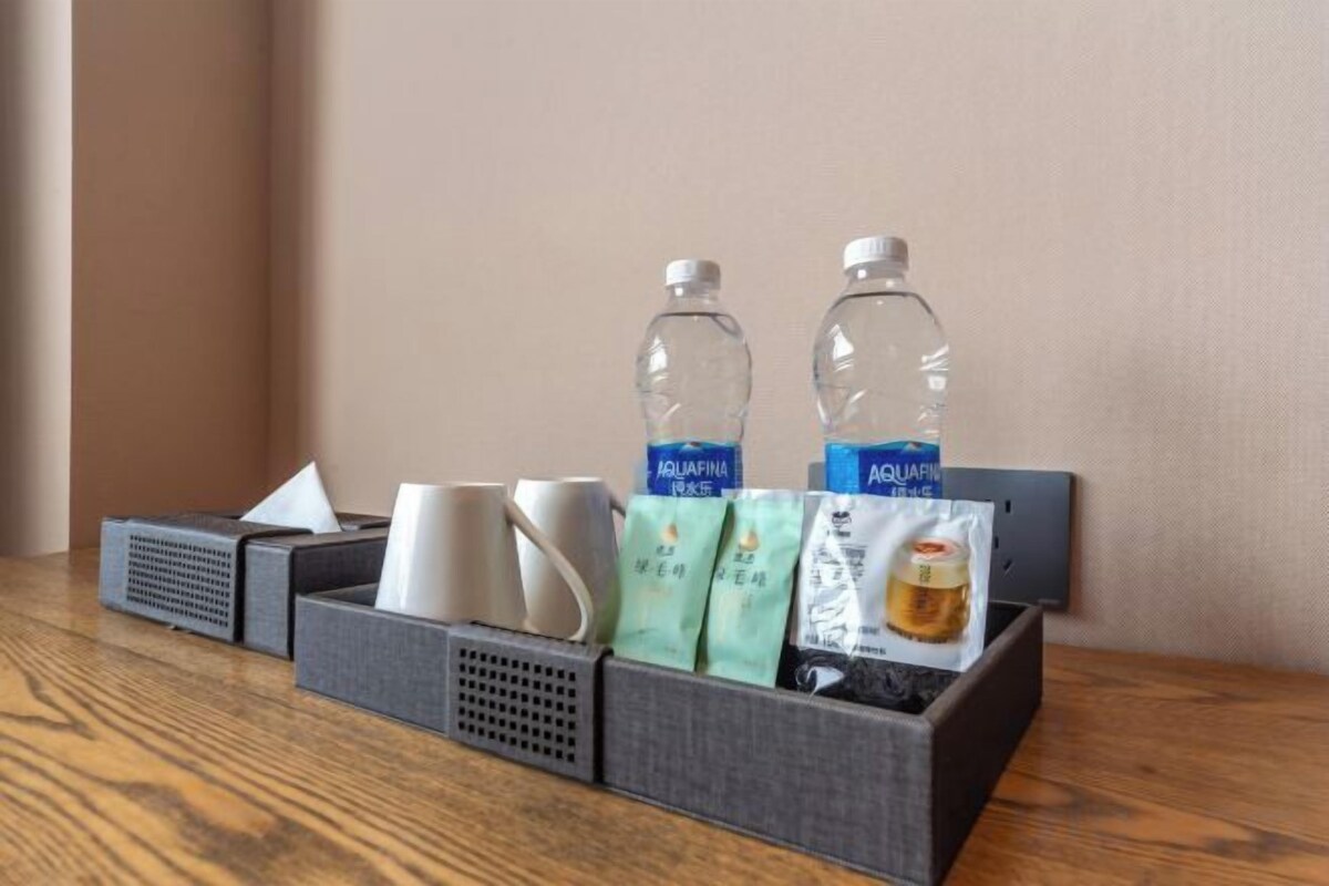 A hotel room's side table with a tissue box, two water bottles, a mug, and a tea bag.
