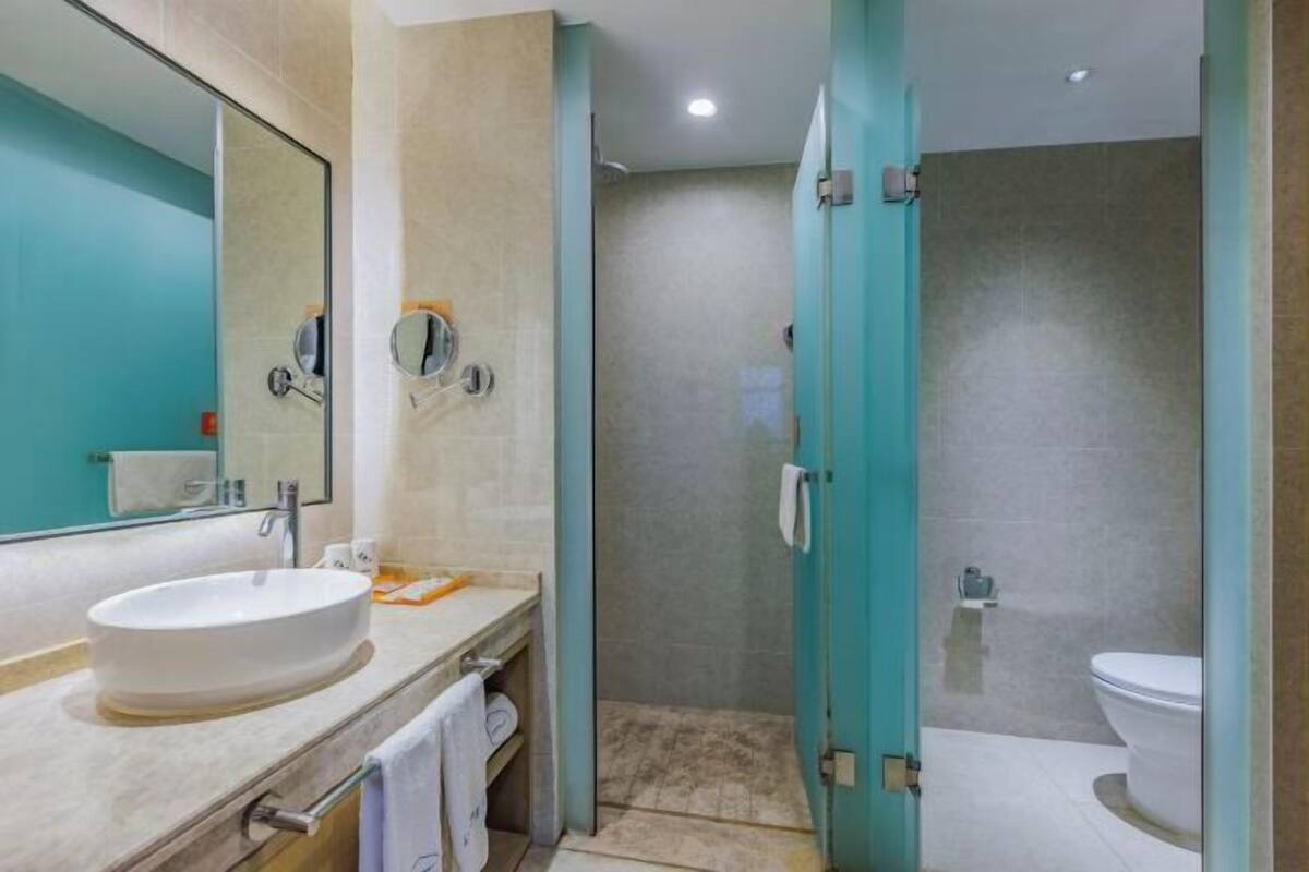 A modern bathroom with a large mirror, a sink, a shower, and a toilet.
