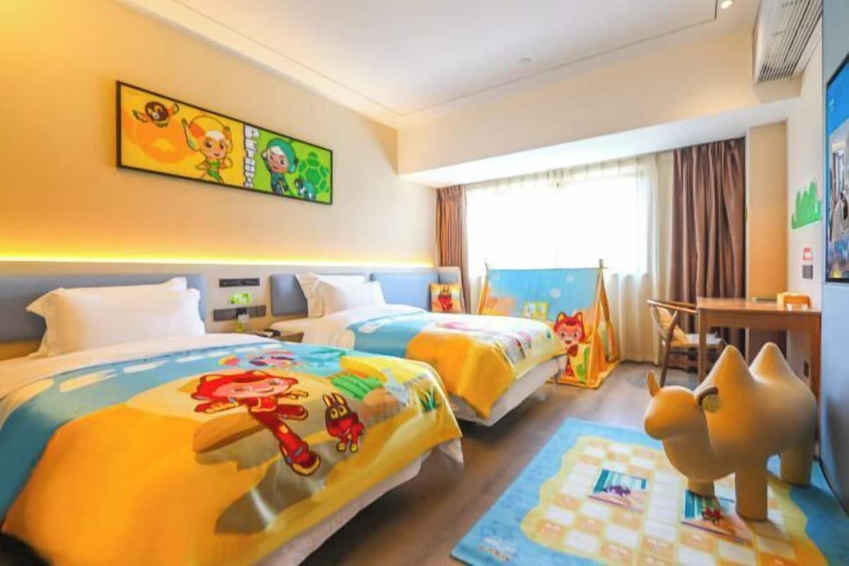 A hotel room with two beds, a desk, a chair, and a large window.