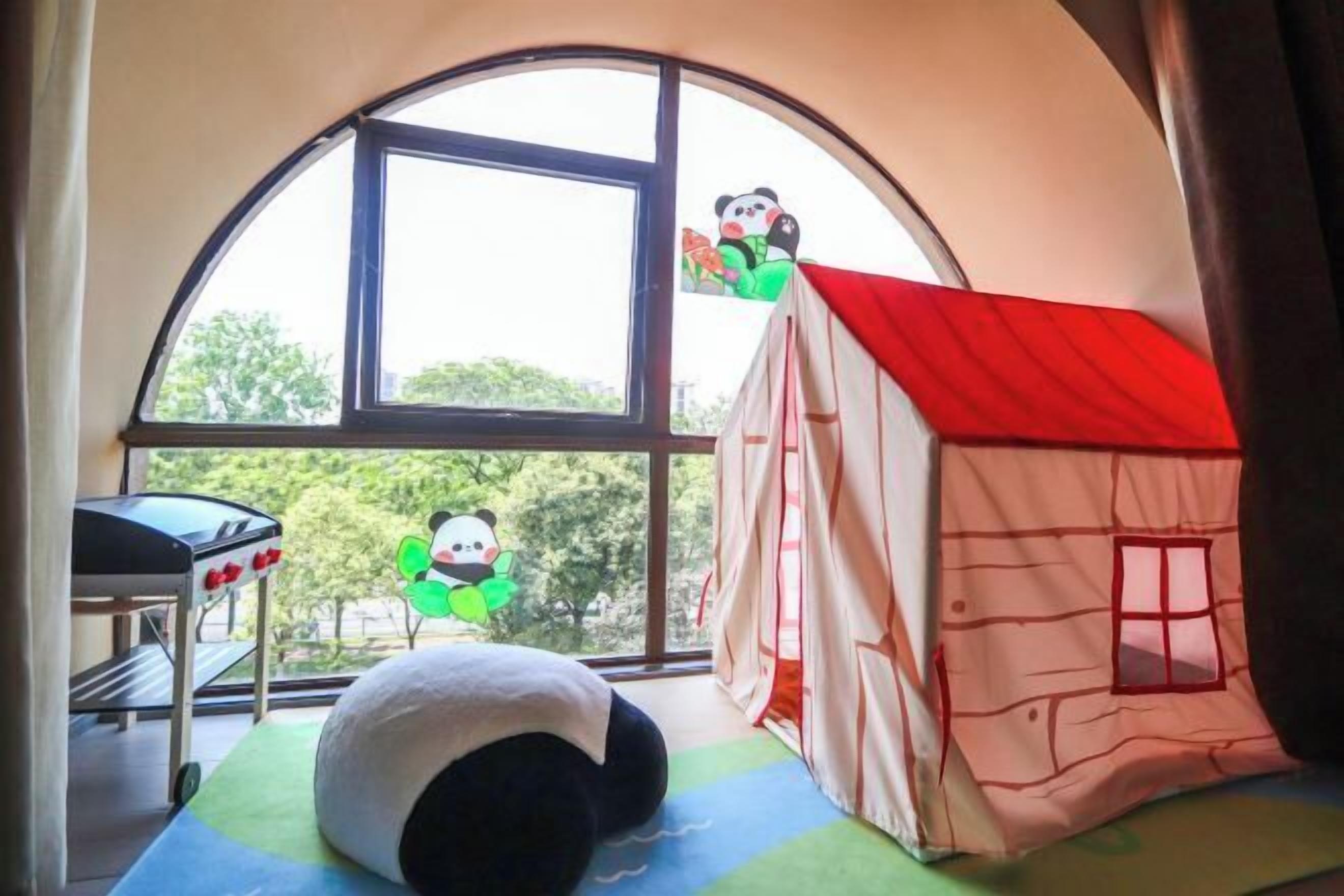 Une pièce dotée d’une grande fenêtre en arc de cercle, d’une maisonnette pour enfants et d’un tapis de course.