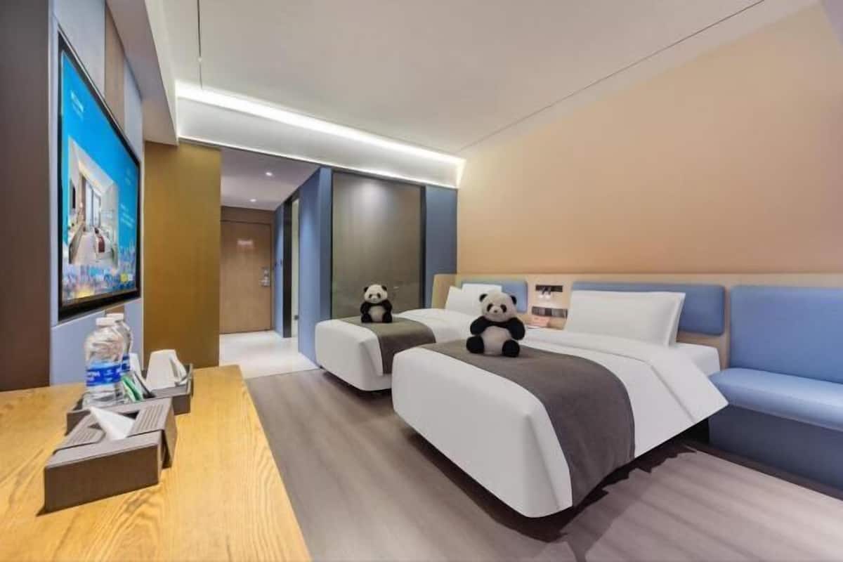 A hotel room with two beds, a TV, a desk, and a panda plush toy on each bed.