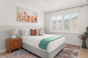 A bedroom with a bed, nightstand, lamp, and a painting on the wall.