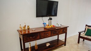 A wooden console table with a television mounted above it, a coffee maker, and various decorative items. - POUSADA DOS GIRASSOIS TRANCOSO (Porto Seguro)
