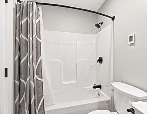 A bathroom with a shower, toilet, and a curved shower curtain.